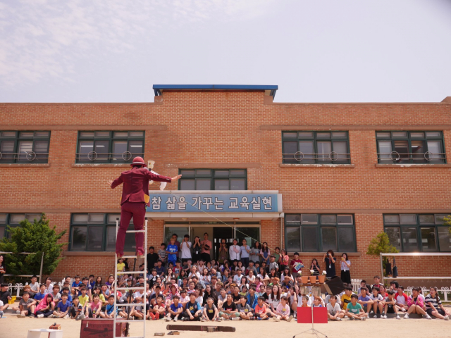 학교 운동장에서 자연과 함께 서커스 공연을 관람하는 아이들